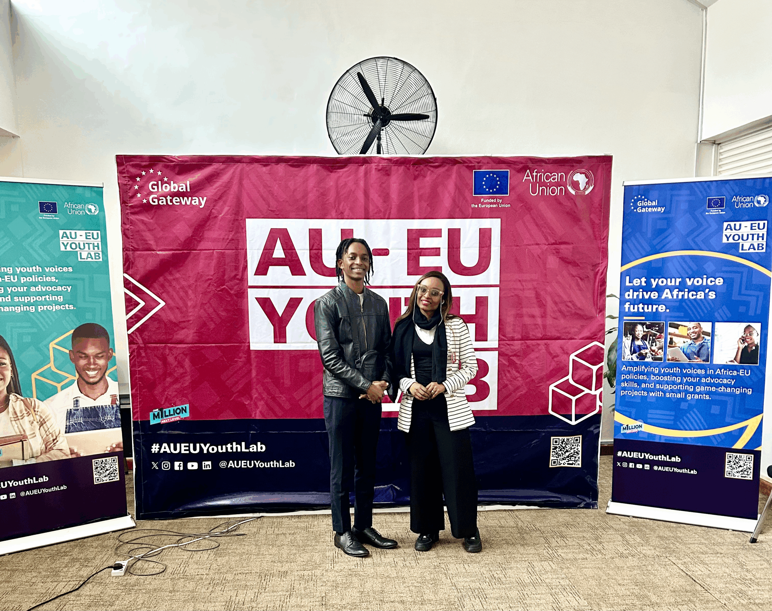 Two people standing in front of a pink banner