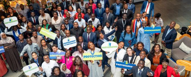 A large group of people pose indoors for a festive group photo celebrating the 10th anniversary of UN Security Council Resolution 2250 on youth, peace, and security.