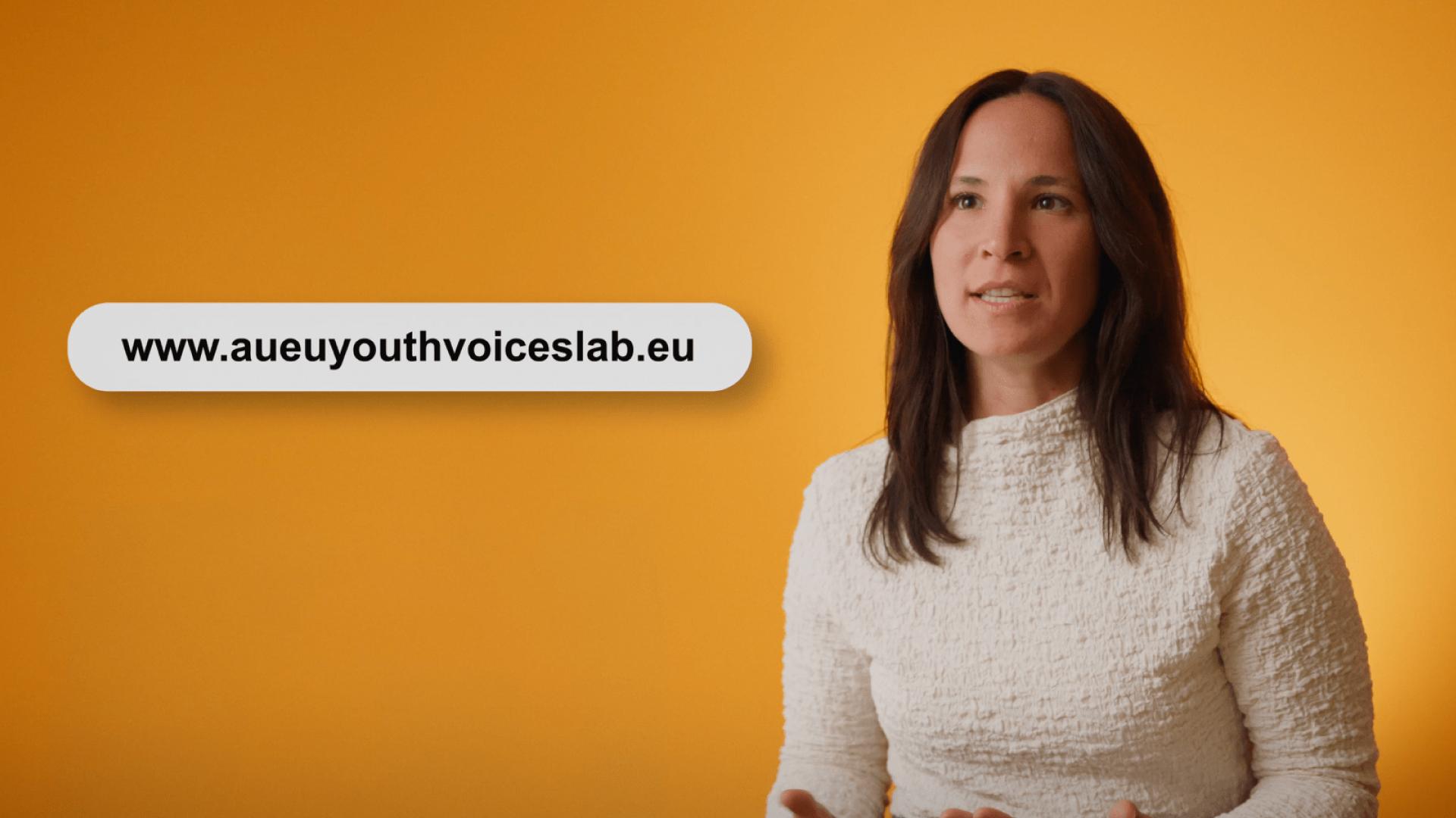 A woman in a white top speaks in front of an orange background. A website URL, www.aueyouthvoiceslab.eu, is displayed in a rounded box to the left of her.