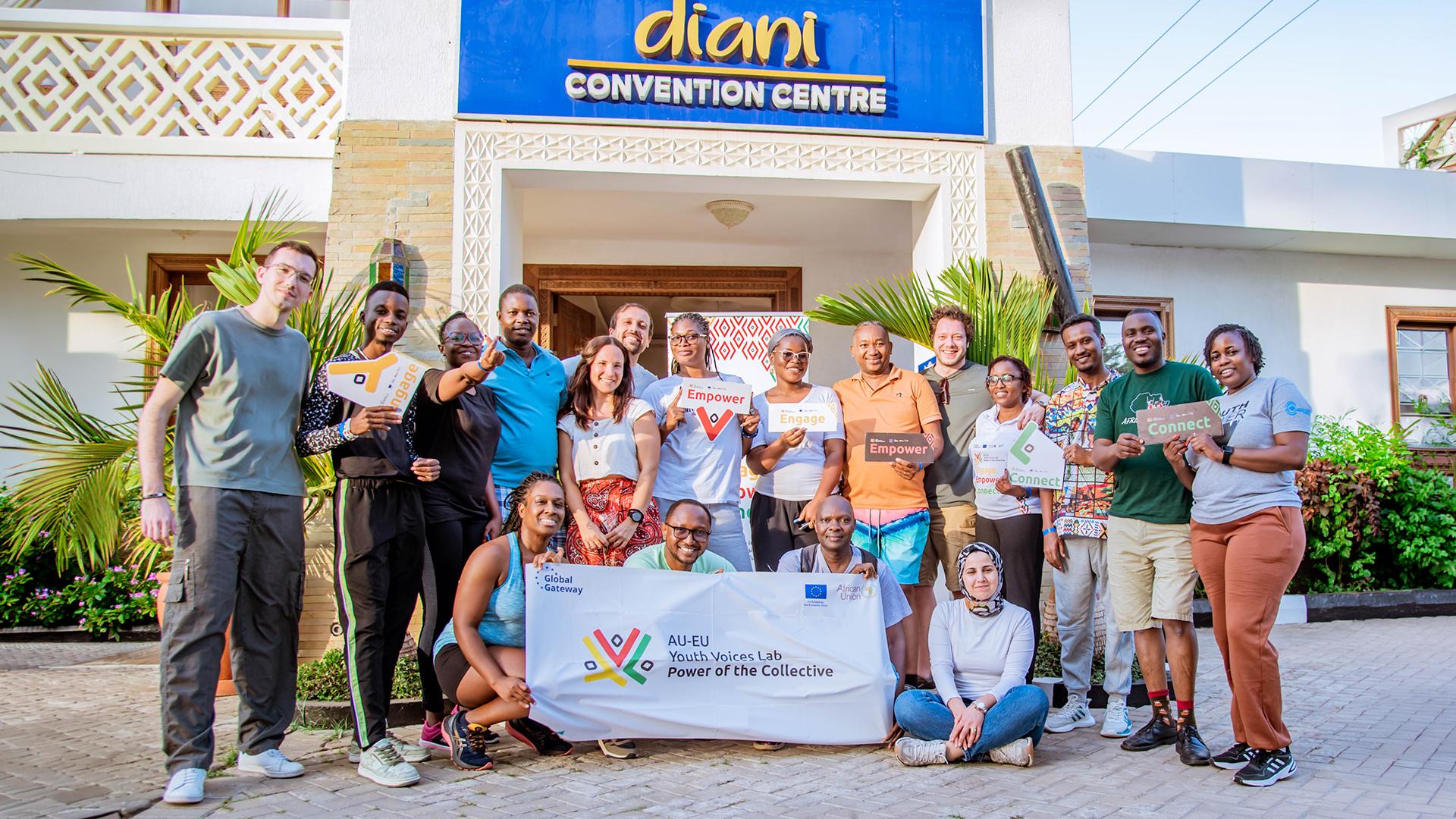 Group of people stand outside the Diani Convention Centre in Kenya. They hold a banner reading “AU–EU Youth Voices Lab: Power of the Collective.
