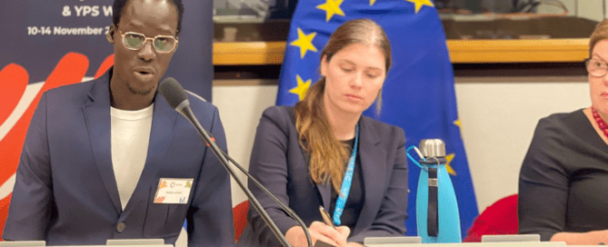 Three panelists seated at a conference table during the Second EU Youth, Peace and Security Conference. Behind them, a banner and European Union flag