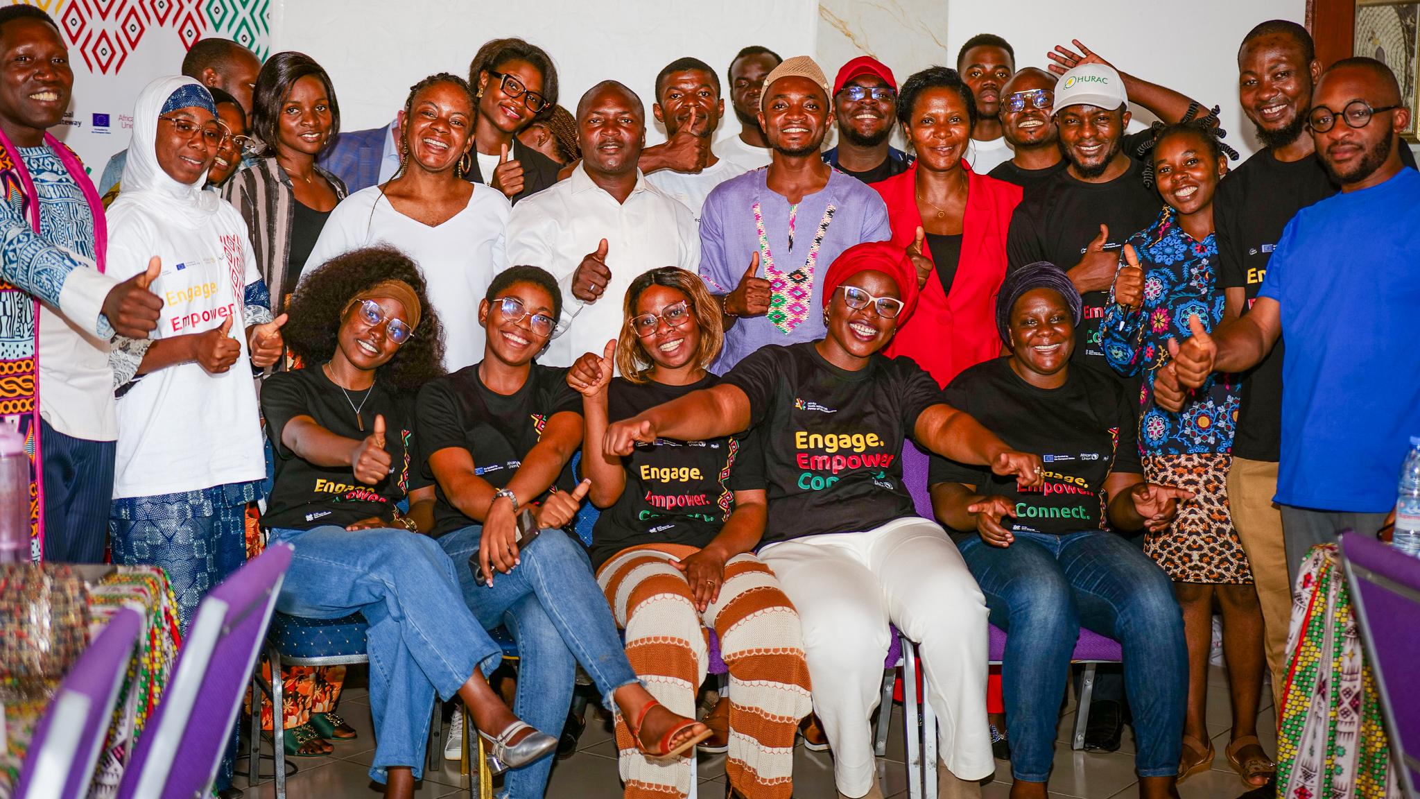 A diverse group of 20 people smiling and posing together indoors, some wearing matching shirts with "Engage, Empower, Connect." The atmosphere is joyful and united.