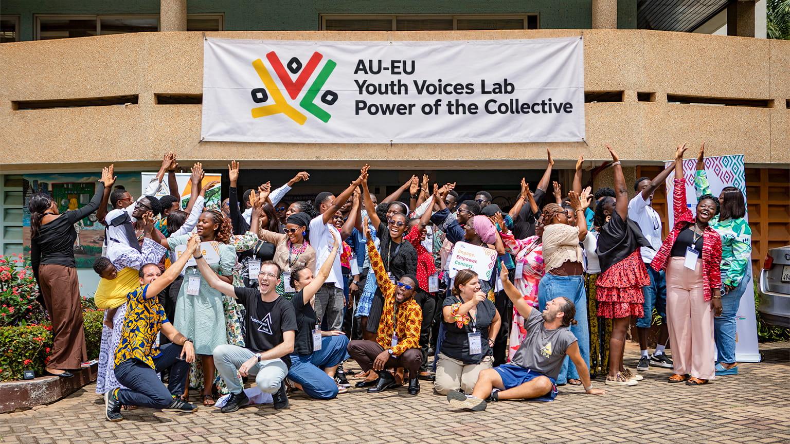 A cheerful group of young adults stands together for a photo, with a building in the background.
