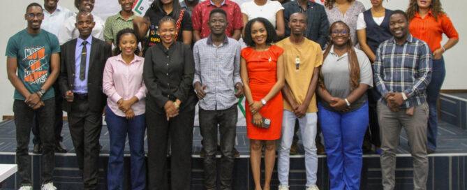 A group of 21 people stands smiling in a well-lit room. They are in casual and formal attire, conveying a sense of professionalism and camaraderie.