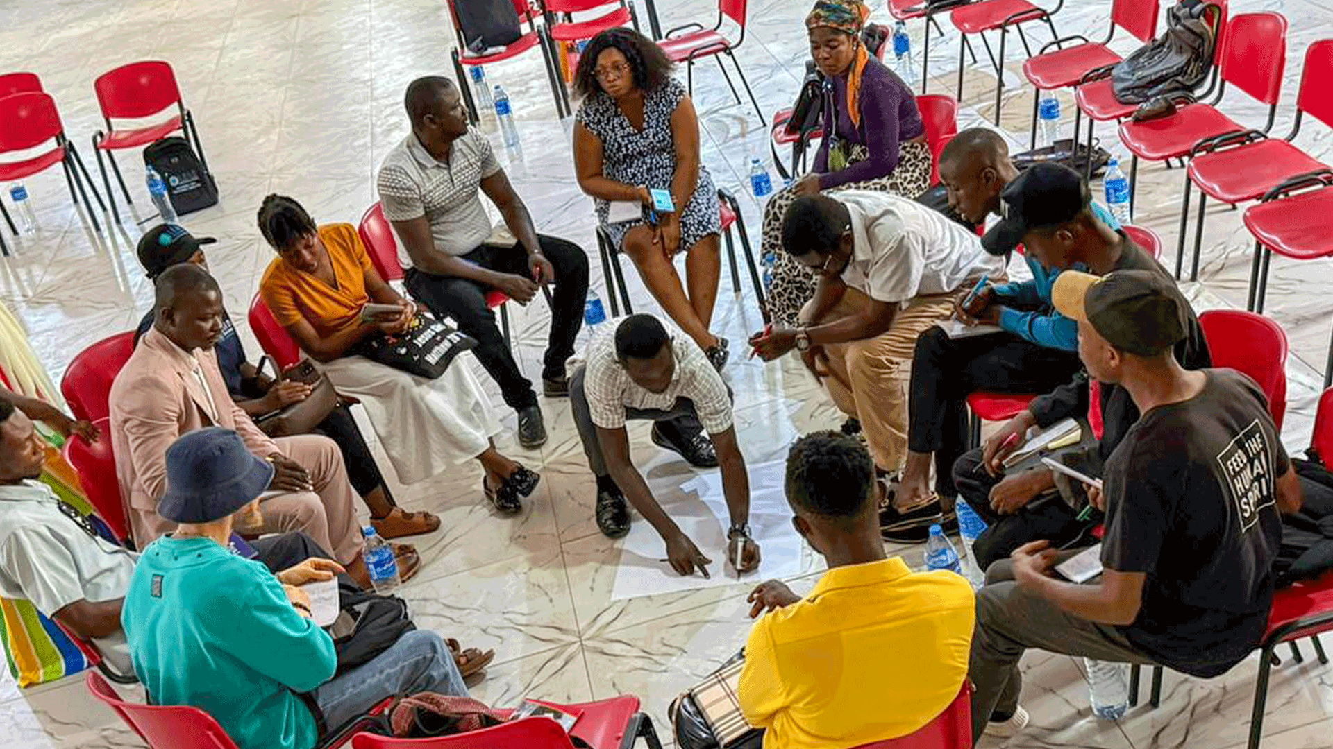 Youth CSO participants sit in a circle during a group discussion, with one participant writing on papers placed on the floor.